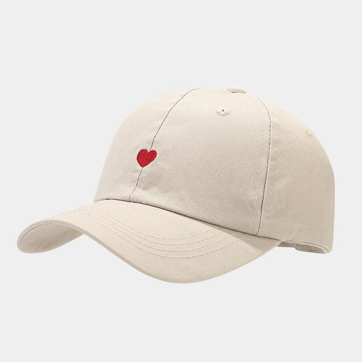 Beige baseball cap with small red heart embroidery on front panel against gray background