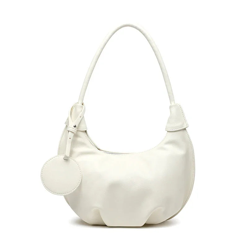 White crescent-shaped leather handbag with single handle and round tag accessory