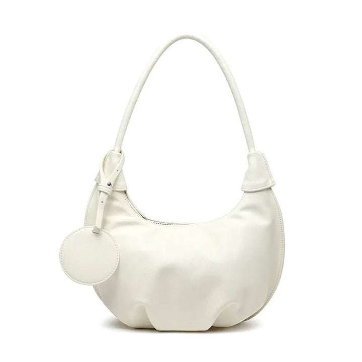 White crescent-shaped leather handbag with single handle and round tag accessory
