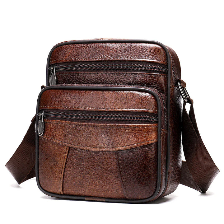 Brown leather crossbody bag with front zippered pockets and adjustable strap on white background