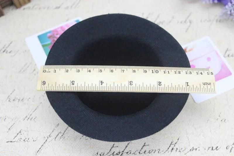 Black round hat with a wooden ruler measuring its diameter on beige fabric background