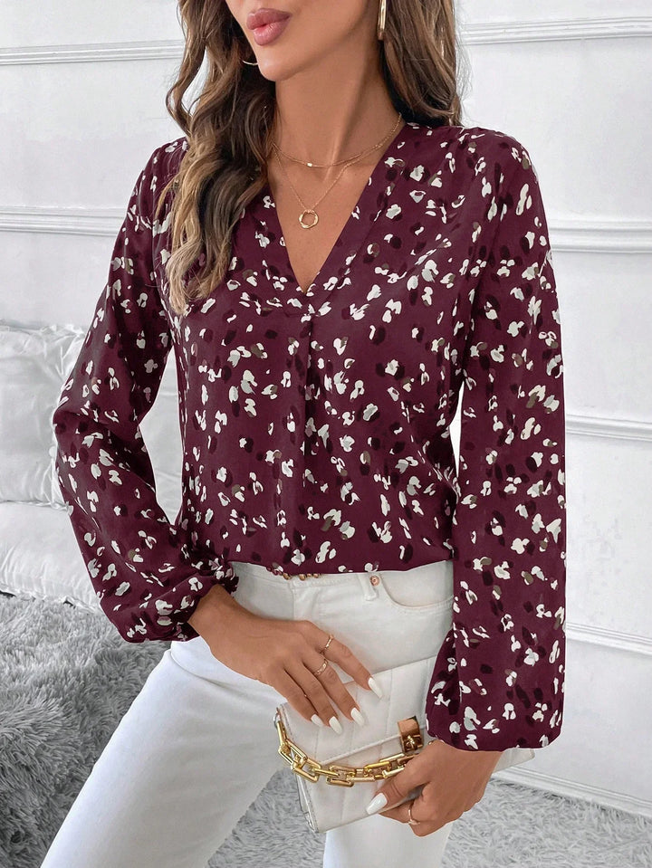 Woman wearing a maroon floral V-neck blouse paired with white pants, holding a white clutch with gold chain detail