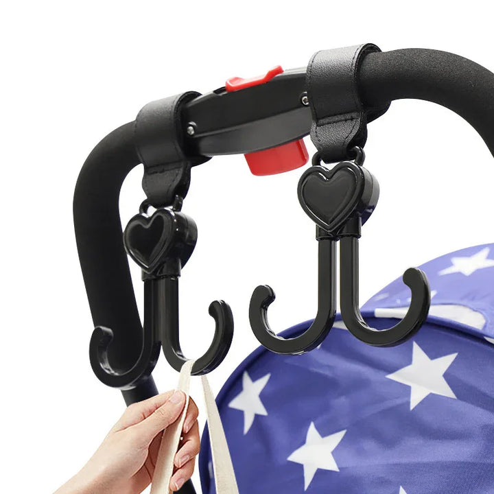 Black double stroller hooks with heart-shaped tops attached to a black stroller handle holding a bag strap