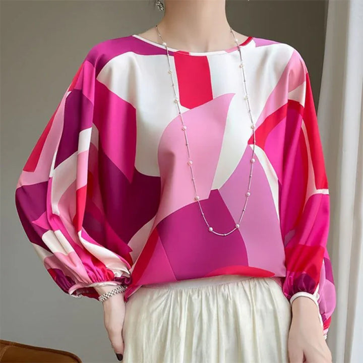 Woman wearing vibrant geometric print blouse with pink, purple, and white tones and billowy sleeves