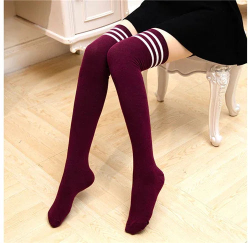 Person wearing maroon thigh-high socks with white stripes sitting on white vintage chair on wooden floor