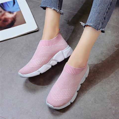 Pink knit slip-on sneakers with white thick soles worn with frayed hem jeans on gray floor