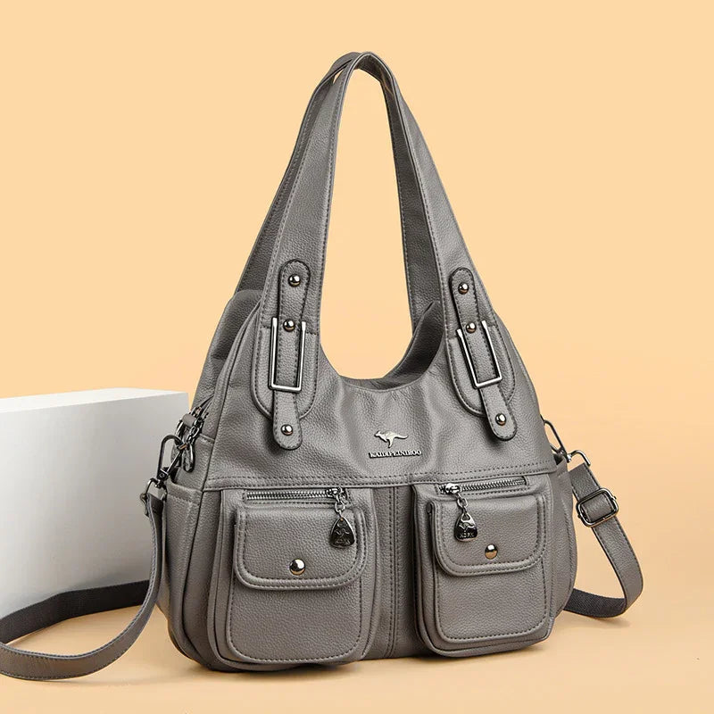 gray leather handbag with double front pockets and adjustable shoulder strap on beige background