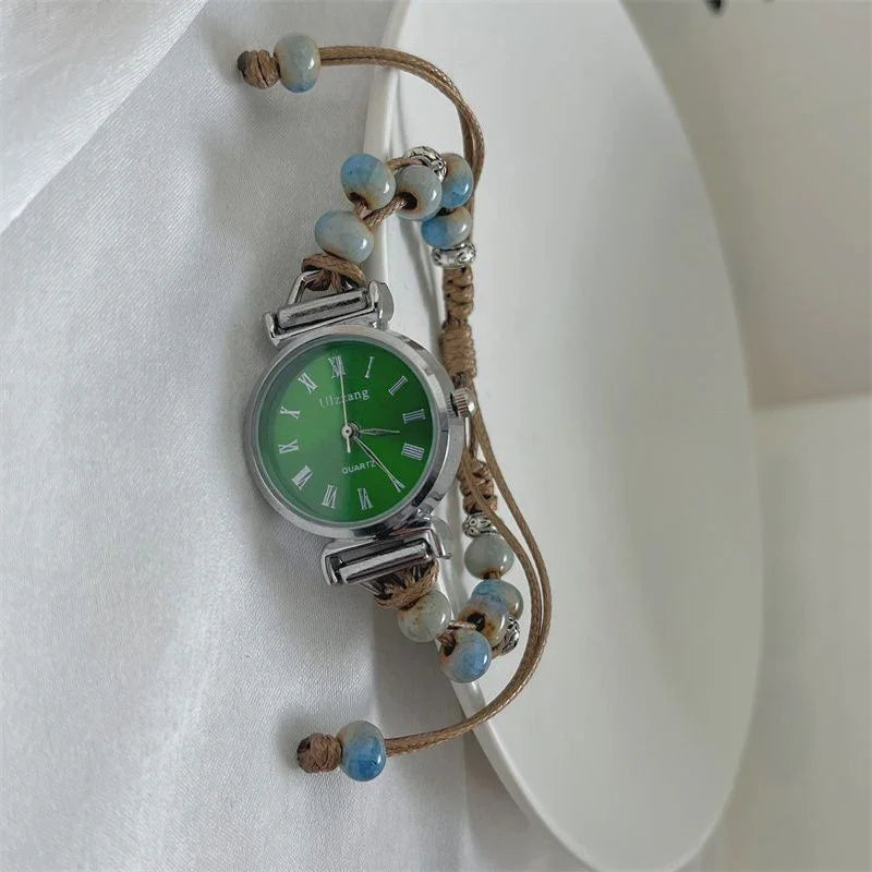Silver quartz wristwatch with green dial, Roman numerals, and beaded brown cord strap