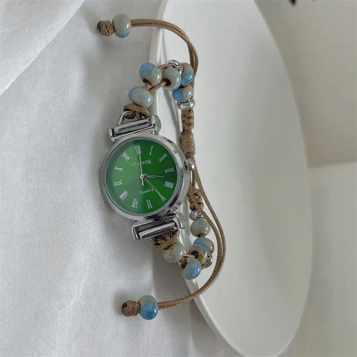 Silver quartz wristwatch with green dial, Roman numerals, and beaded brown cord strap