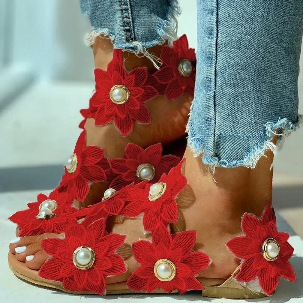 Trendy open-toe sandals with red flower appliques and pearl centers worn with frayed blue jeans