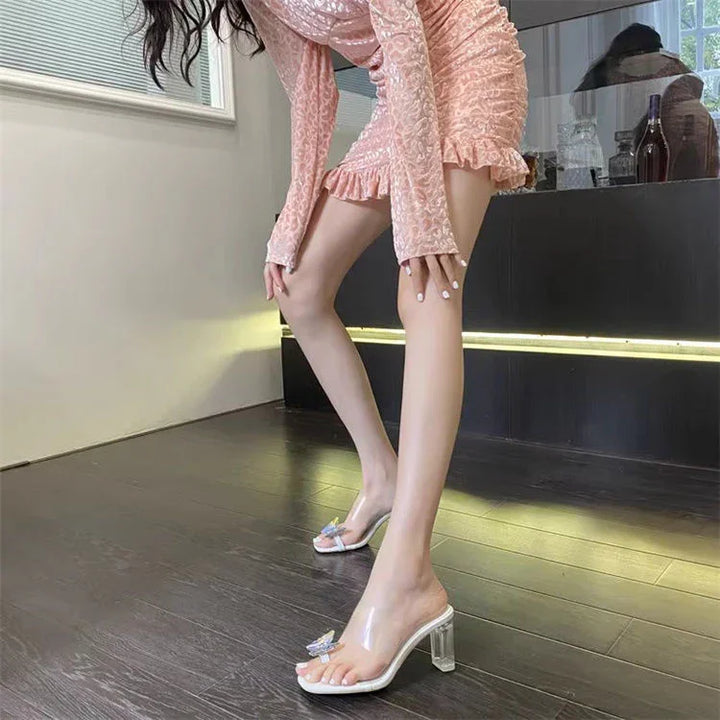 Woman wearing pink ruched dress and clear high-heeled sandals with butterfly detail indoors