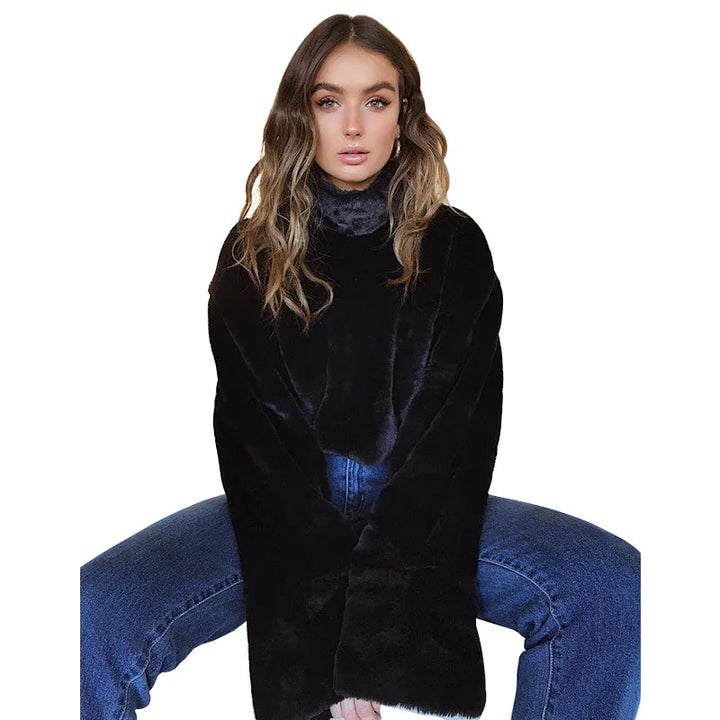 Young woman wearing black faux fur jacket and blue jeans sitting with legs apart on white background