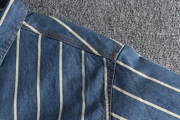 close-up of blue denim fabric with white vertical stripes and detailed stitching on gray textile background