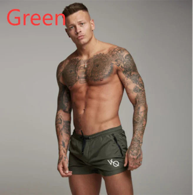 Tattooed muscular man wearing green shorts with VO logo posing against gray background