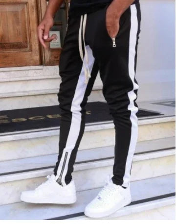 Black jogger pants with white side stripes, drawstring, zipper detail, white sneakers