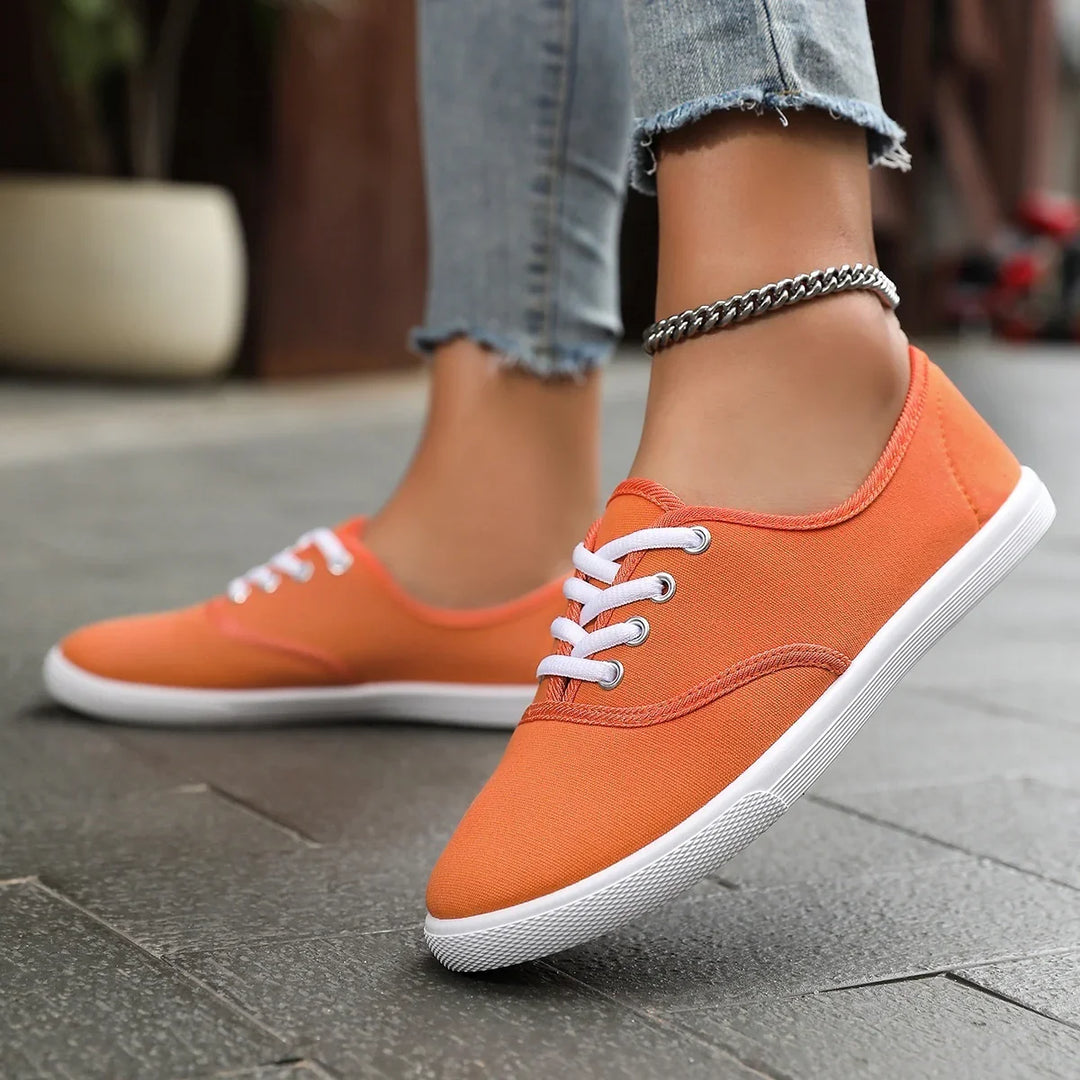 Close-up of feet wearing orange canvas sneakers with white laces and ankle chain on urban pavement