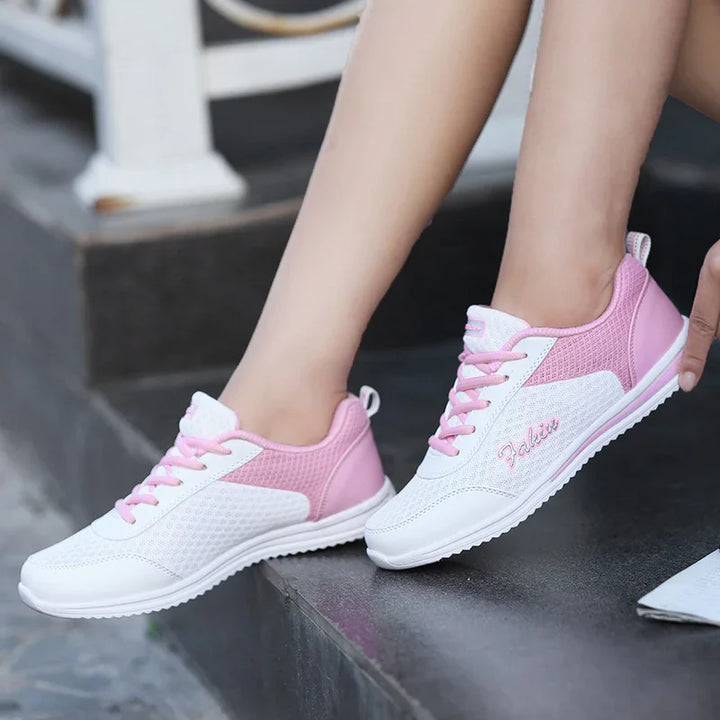 White and pink lightweight sneakers worn on feet, sitting on black stone steps, casual shoes