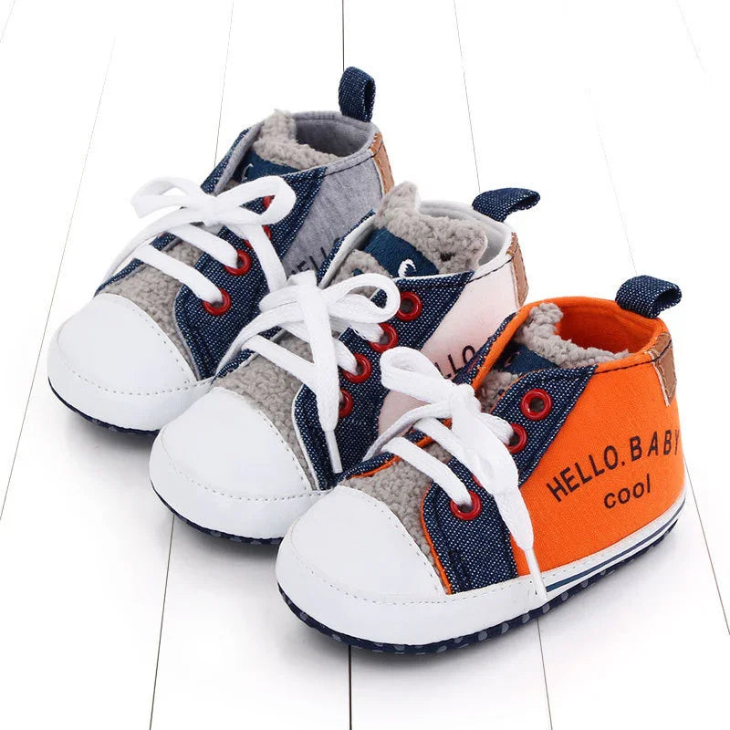 Three pairs of baby shoes in gray, blue, and orange with white laces and fleece lining on white wooden floor