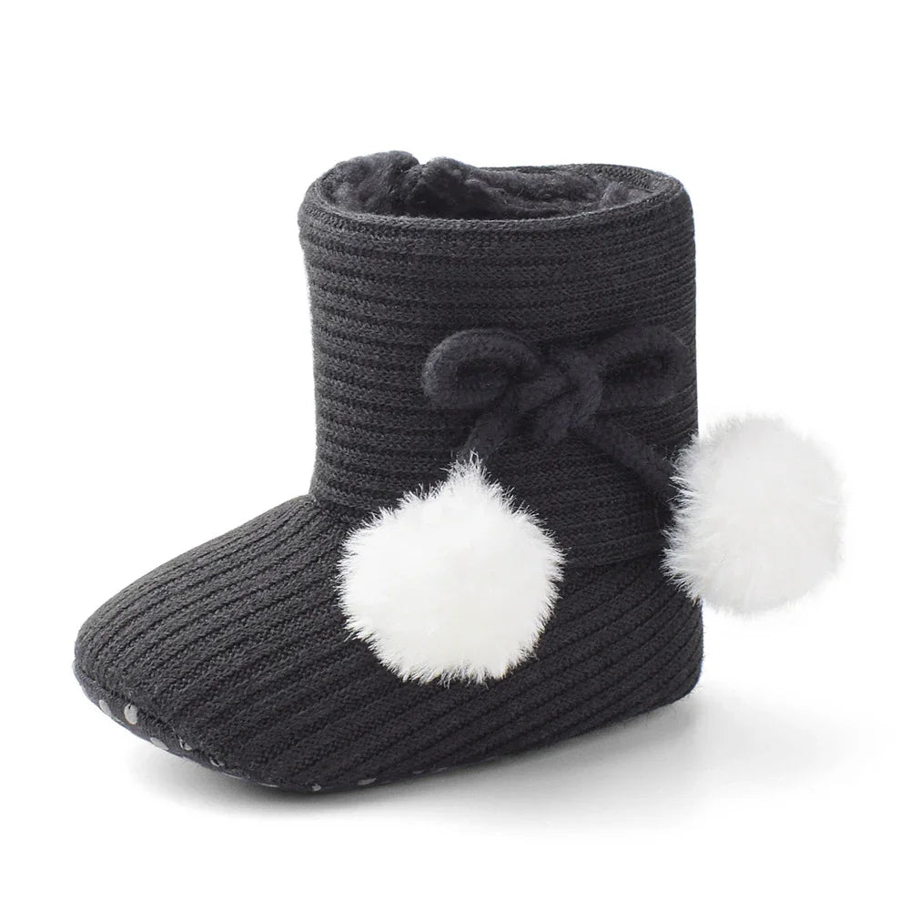 Black knitted baby bootie with fluffy white pom-poms and cozy interior lining