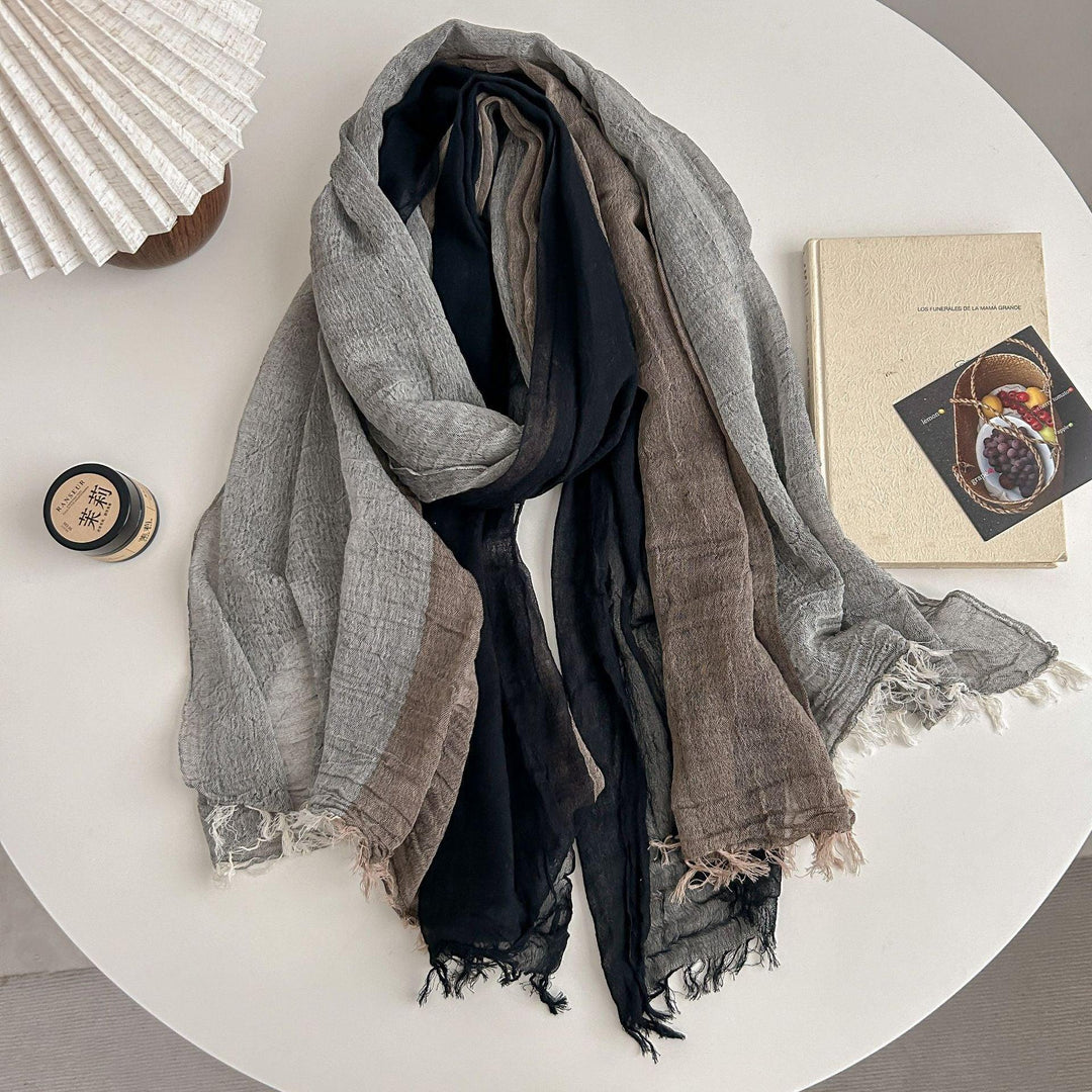 Soft textured scarf in black, gray, and brown hues displayed on white round table with book and candle