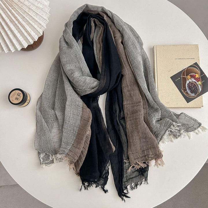 Soft textured scarf in black, gray, and brown hues displayed on white round table with book and candle
