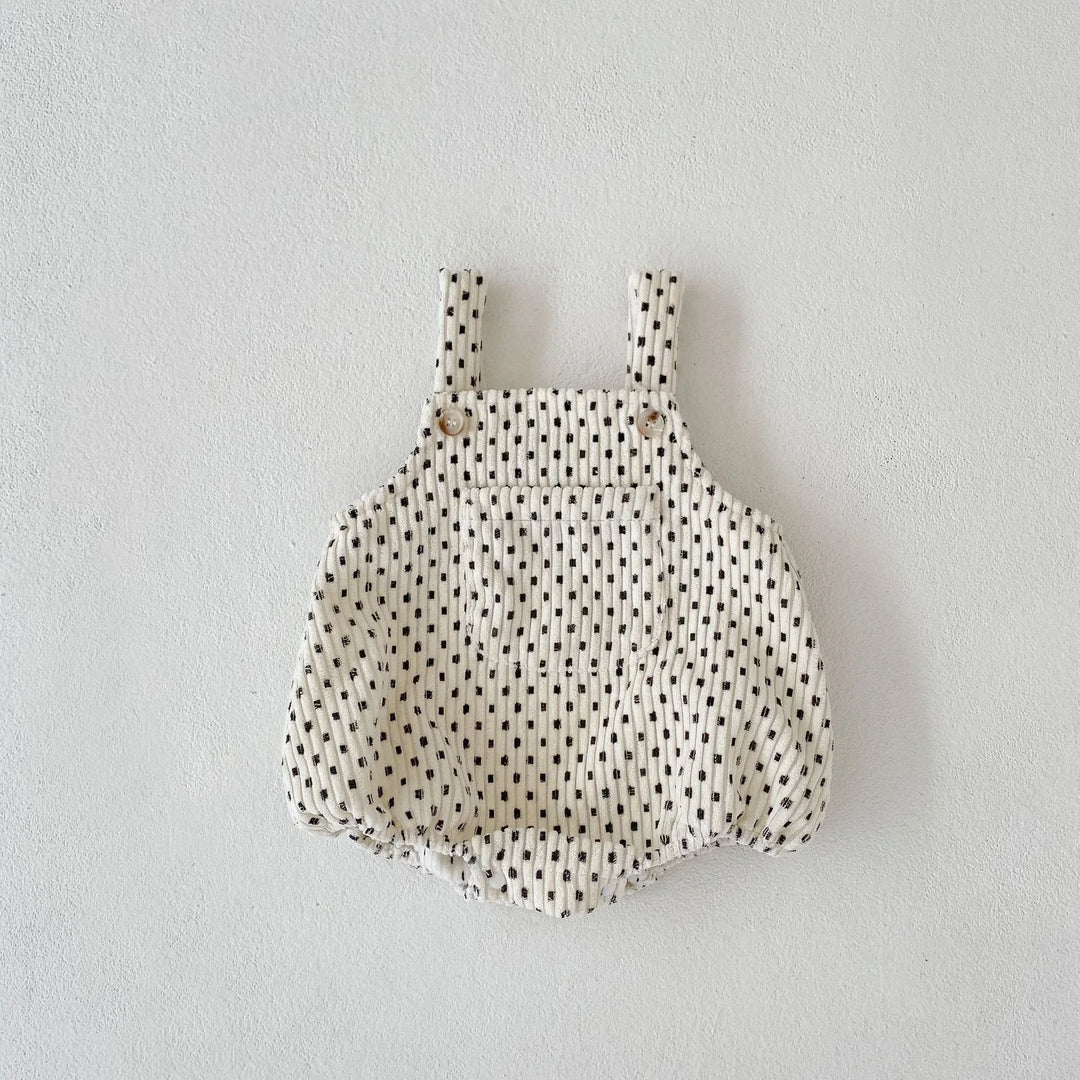 Cream baby romper with black dotted pattern and buttoned shoulder straps on white background
