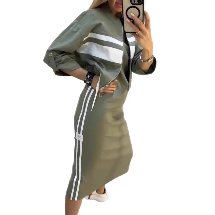 Woman in olive green sporty two-piece outfit with white stripes, holding phone, wearing white sneakers