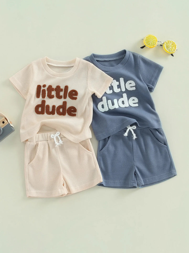Two toddler waffle knit short sets with 'little dude' text, one beige with brown letters, one blue with white letters