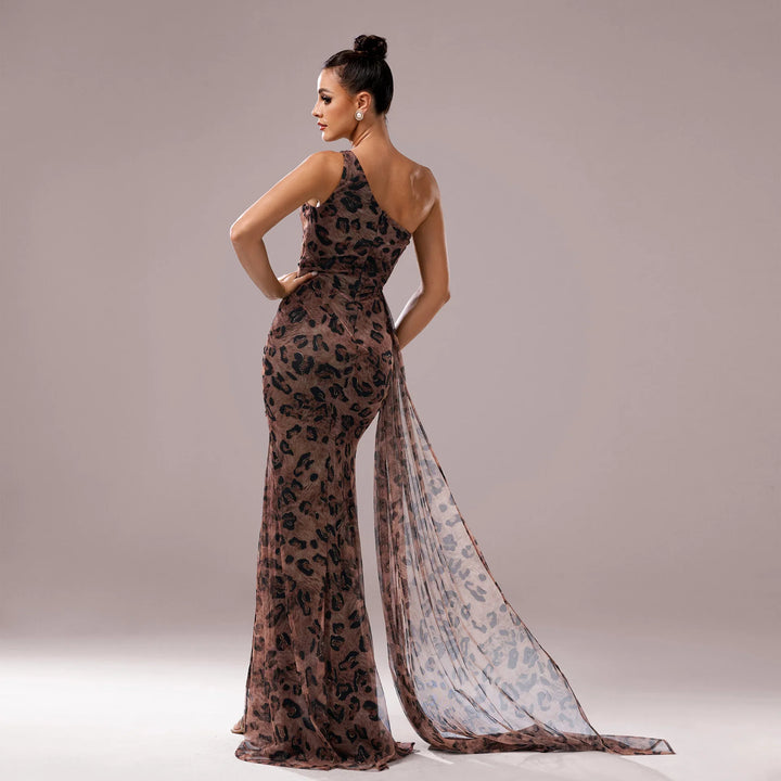 Woman in a one-shoulder leopard print evening gown with sheer trailing fabric on plain background