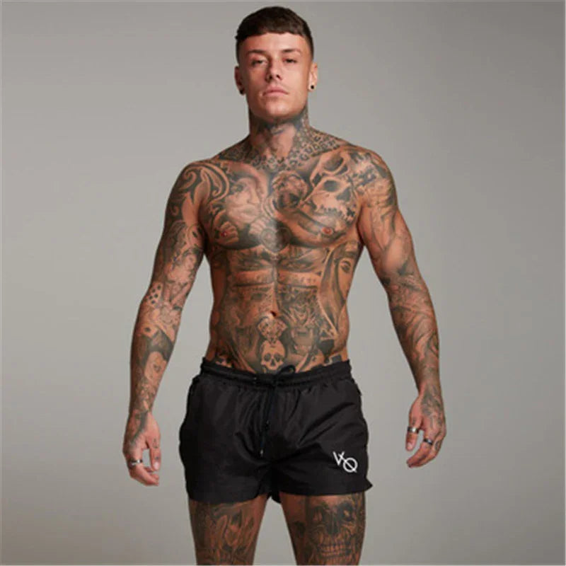 muscular tattooed man wearing black shorts posing against gray background