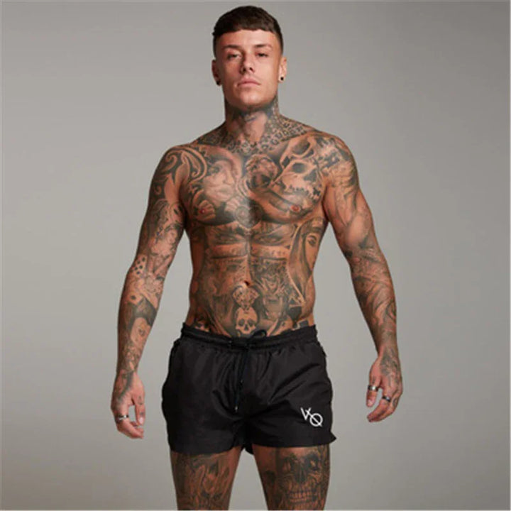 muscular tattooed man wearing black shorts posing against gray background