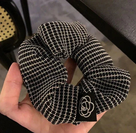 Hand holding black and white checkered fabric scrunchie with a small logo tag against blurred background