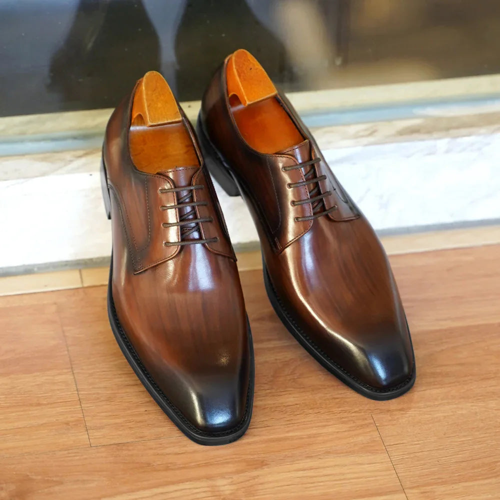 Pair of polished brown leather dress shoes on wooden floor near glass door