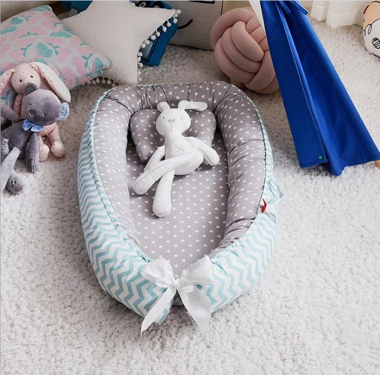 Baby lounger with gray star pattern and white bow, featuring a soft white rabbit toy inside on a cozy carpet