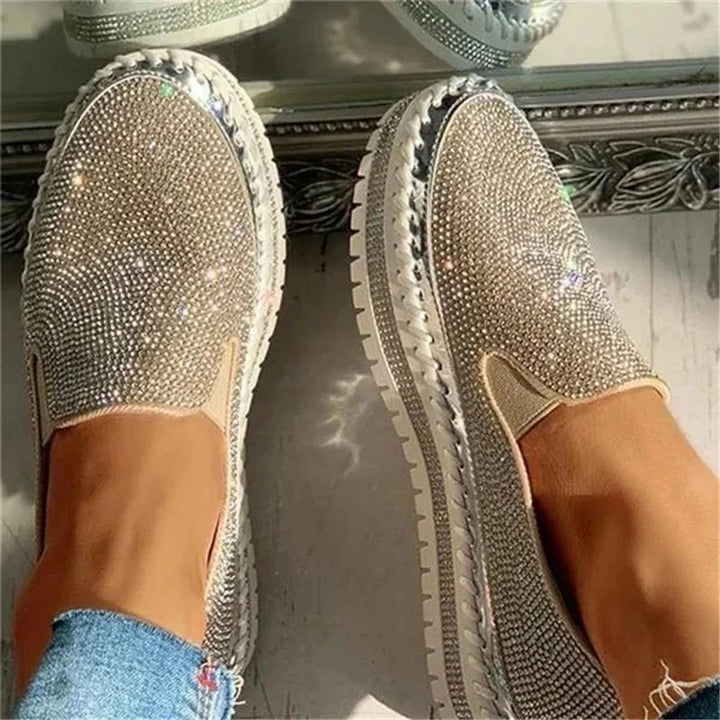 close-up of feet wearing slip-on platform shoes studded with silver rhinestones on light floor with a decorative mirror