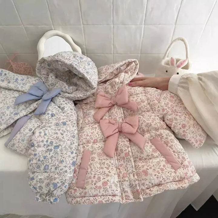 Two floral-patterned baby jackets with bows, one pink and one blue, on a white surface