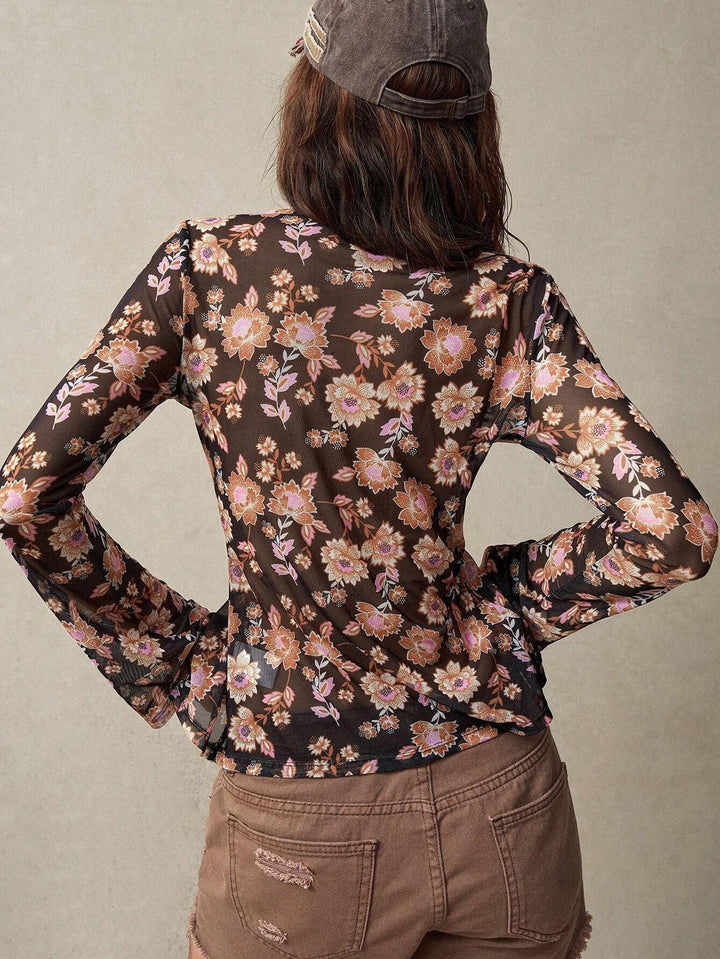 Back view of woman wearing sheer black floral long-sleeve top and distressed brown shorts with a gray cap
