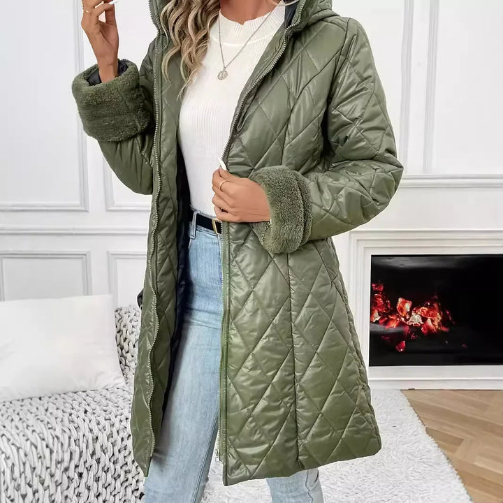 Woman wearing quilted olive green winter coat with faux fur cuffs and white sweater indoors