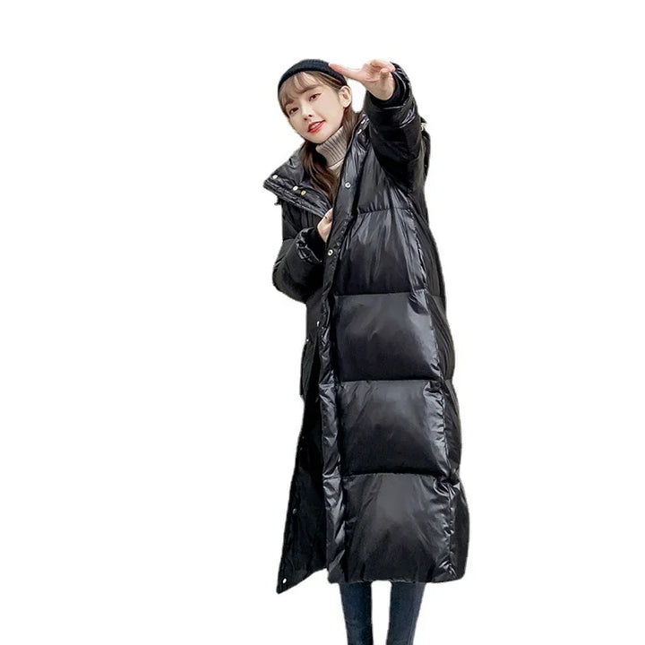 Young woman in black long puffer coat, beige turtleneck sweater, and black beanie posing with hand raised