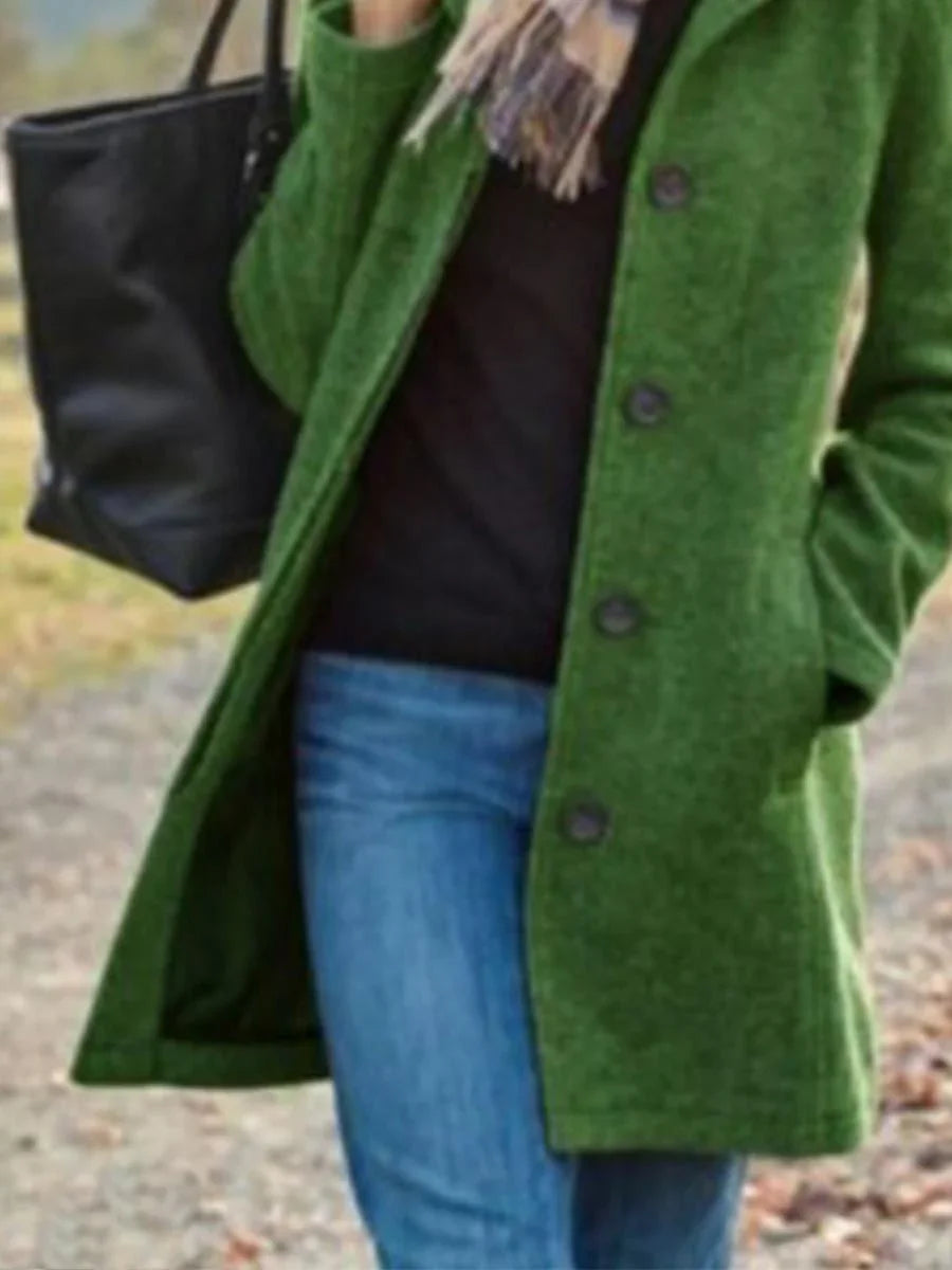 Person wearing a green buttoned coat, blue jeans, black top, scarf, and carrying a black tote bag