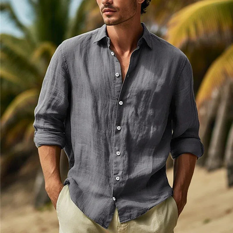 Man wearing gray linen button-up shirt and beige pants standing outdoors with palm trees in background