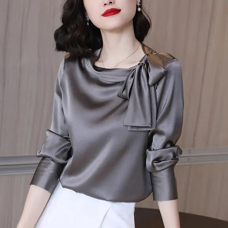 Woman wearing elegant gray satin blouse with bow detail and ruched sleeves, paired with white skirt