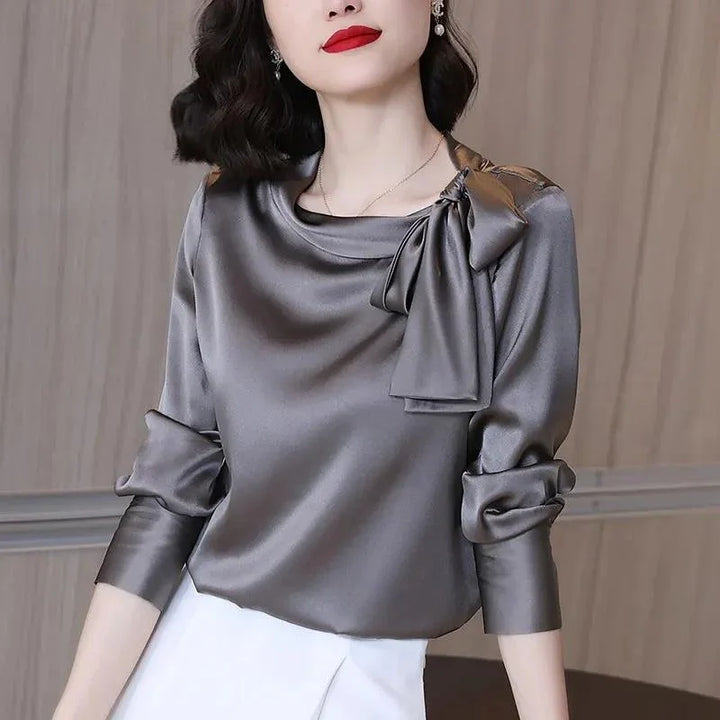 Woman wearing elegant gray satin blouse with bow detail and ruched sleeves, paired with white skirt