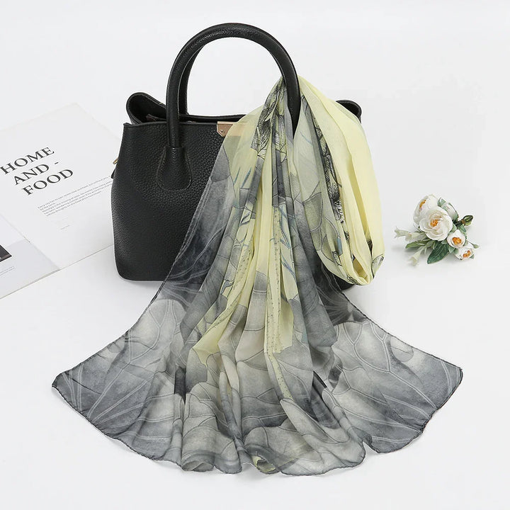 Black leather handbag with a flowing sheer floral scarf in yellow and gray tones, on white background