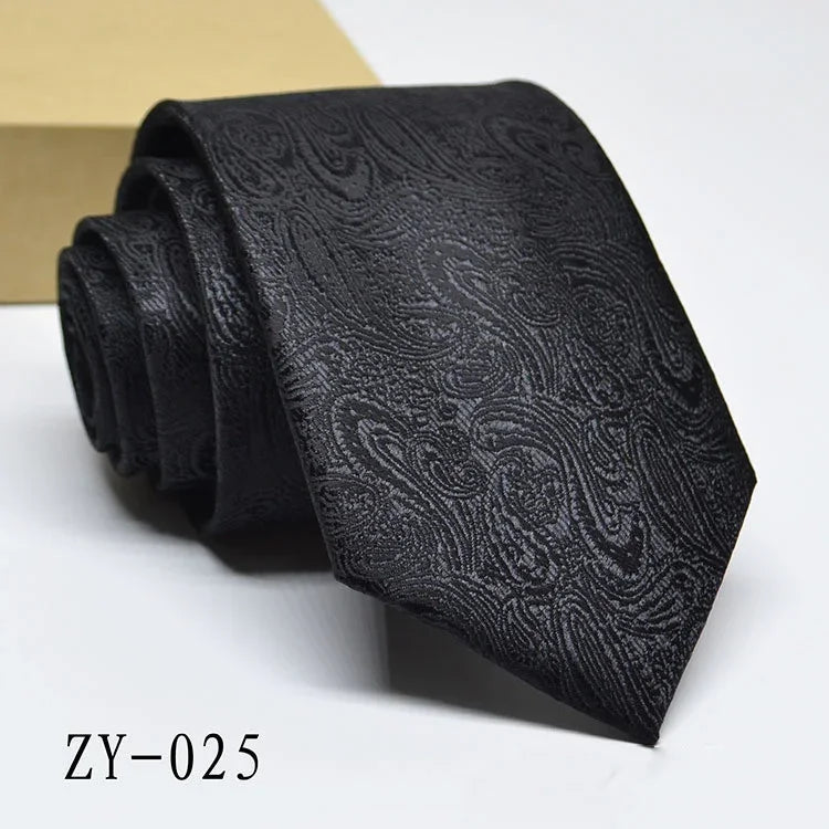 Black paisley patterned necktie rolled on white surface with beige background