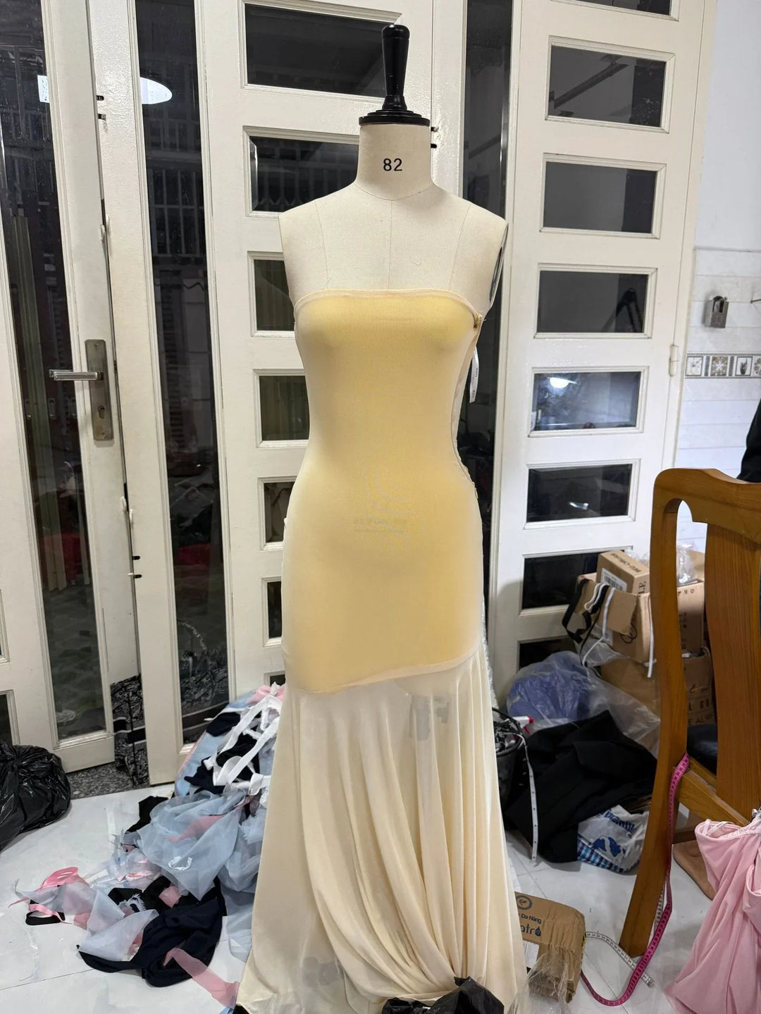 Beige strapless fitted dress on mannequin in a room with sewing materials and white glass-paneled doors