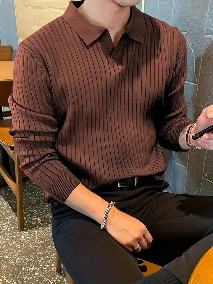 Man wearing brown ribbed knit sweater with collar and black pants sitting indoors