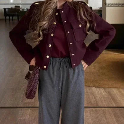 Woman wearing a dark burgundy jacket and top with high-waisted gray pants indoors