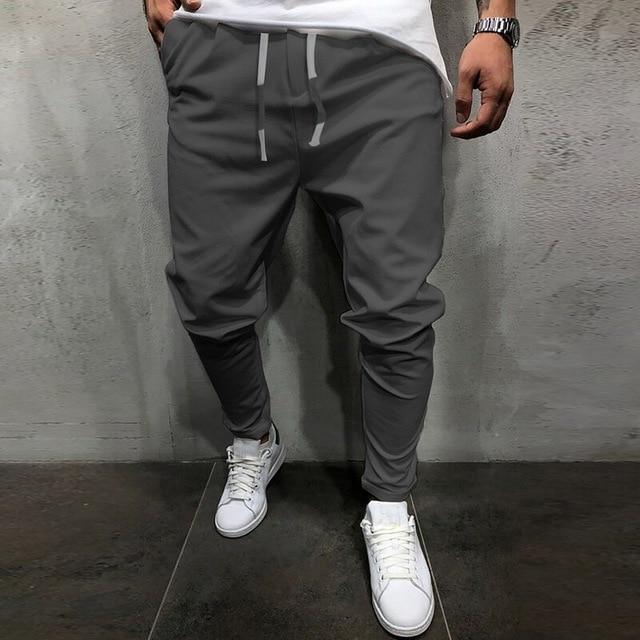 Man wearing gray jogger pants with white drawstrings and white sneakers against a concrete wall
