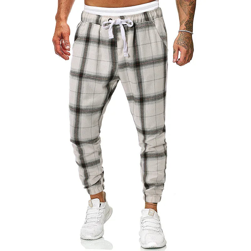 Men's gray and white plaid jogger pants with white drawstring and elastic cuffs, worn with white sneakers